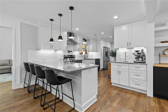 kitchen featuring light stone counters, wood finished floors, a peninsula, white cabinets, and appliances with stainless steel finishes