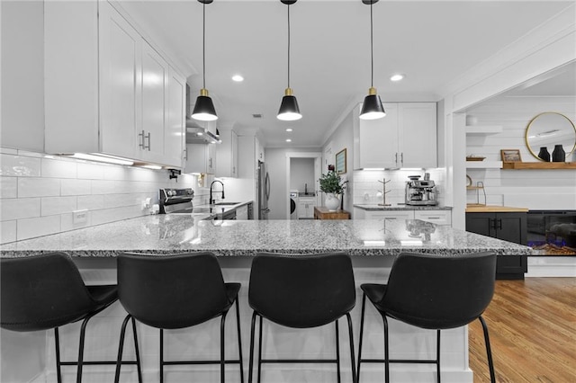 kitchen with washing machine and dryer, a peninsula, white cabinetry, and crown molding