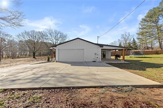 view of property exterior with a lawn, a trampoline, fence, concrete driveway, and an attached garage