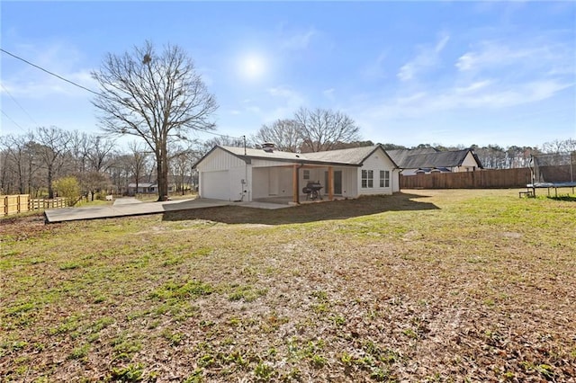 view of yard featuring a patio area, a trampoline, an attached garage, and fence