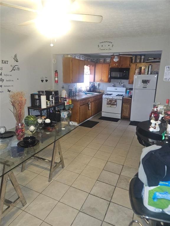 kitchen featuring white appliances, light tile patterned floors, brown cabinetry, and a ceiling fan