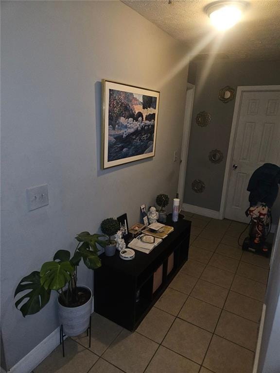 corridor featuring light tile patterned flooring, a textured ceiling, and baseboards