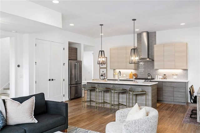 kitchen featuring high end fridge, modern cabinets, wall chimney range hood, light countertops, and a sink