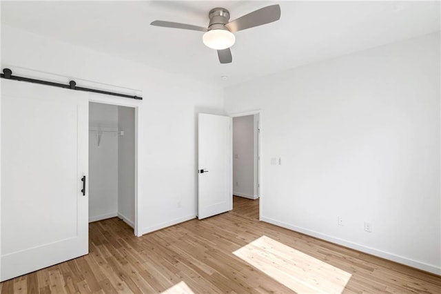 unfurnished bedroom with ceiling fan, a barn door, baseboards, wood finished floors, and a closet
