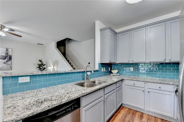 kitchen featuring a sink, dishwasher, light wood-style flooring, backsplash, and gray cabinetry