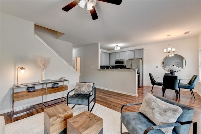 living area with visible vents, wood finished floors, stairway, baseboards, and ceiling fan with notable chandelier