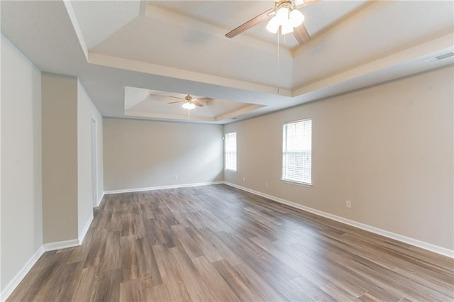 unfurnished room with ceiling fan, a raised ceiling, and wood-type flooring