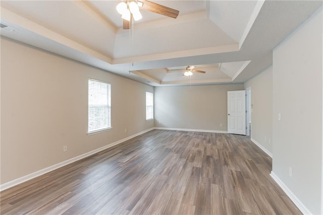 empty room featuring ceiling fan, wood-type flooring, and a tray ceiling