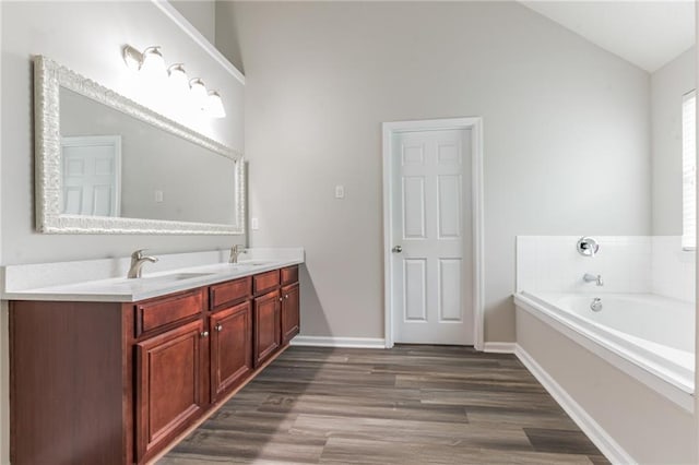 bathroom featuring hardwood / wood-style floors, a bathing tub, double sink vanity, and lofted ceiling