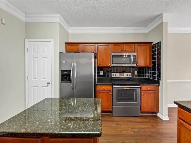 kitchen featuring crown molding, dark stone countertops, backsplash, stainless steel appliances, and dark hardwood / wood-style floors