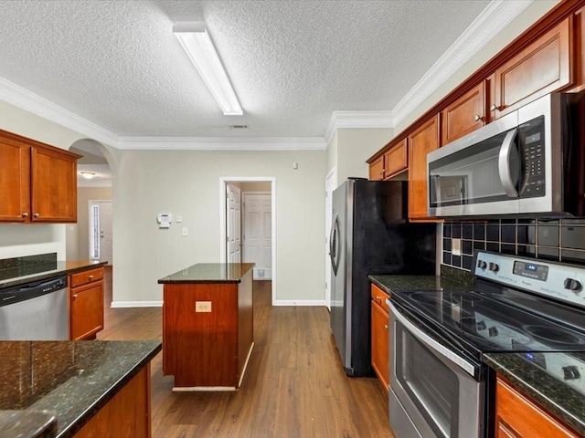 kitchen with stainless steel appliances, wood-type flooring, a center island, and dark stone countertops