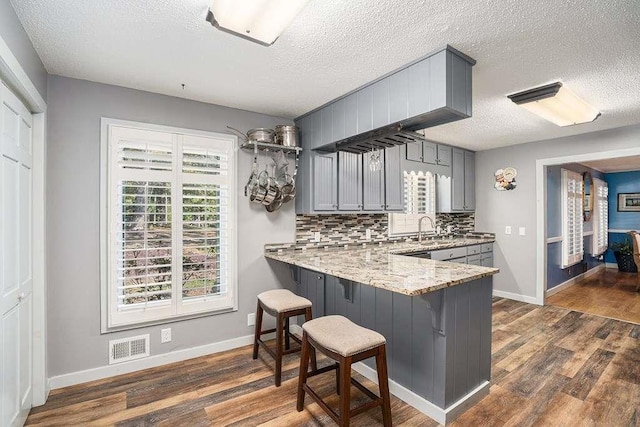 kitchen featuring sink, gray cabinets, tasteful backsplash, dark hardwood / wood-style flooring, and kitchen peninsula