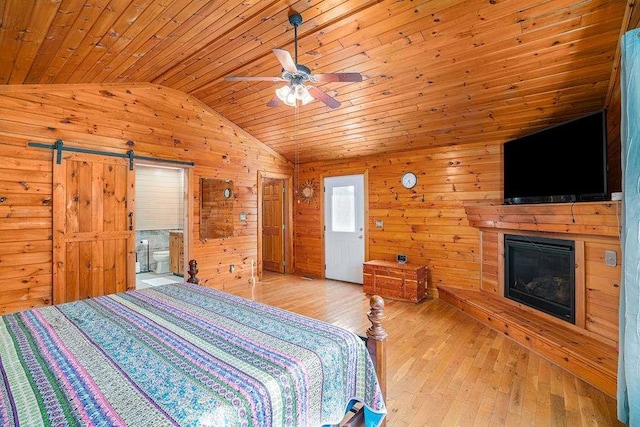 bedroom with a barn door, light hardwood / wood-style floors, vaulted ceiling, and wooden ceiling