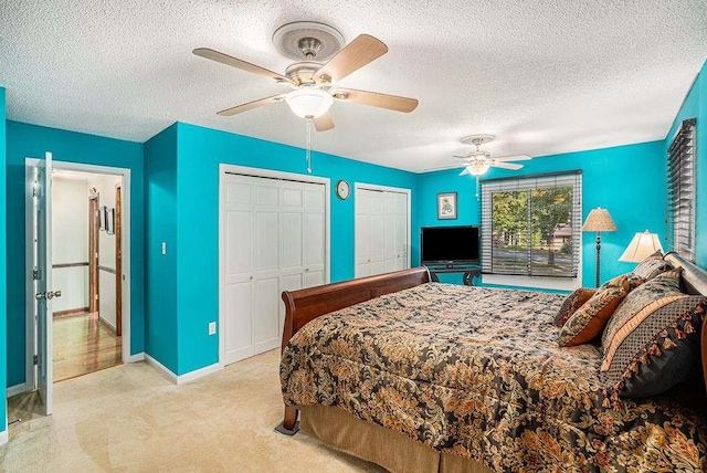 carpeted bedroom with ceiling fan, two closets, and a textured ceiling