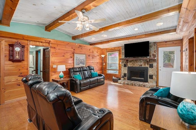 living room featuring ceiling fan, vaulted ceiling with beams, wooden walls, a fireplace, and light hardwood / wood-style floors