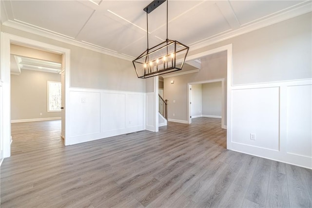 unfurnished dining area featuring beam ceiling, a chandelier, wood-type flooring, and ornamental molding