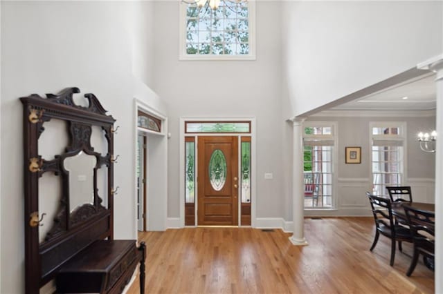 entryway with a notable chandelier, light wood-style floors, a high ceiling, crown molding, and ornate columns