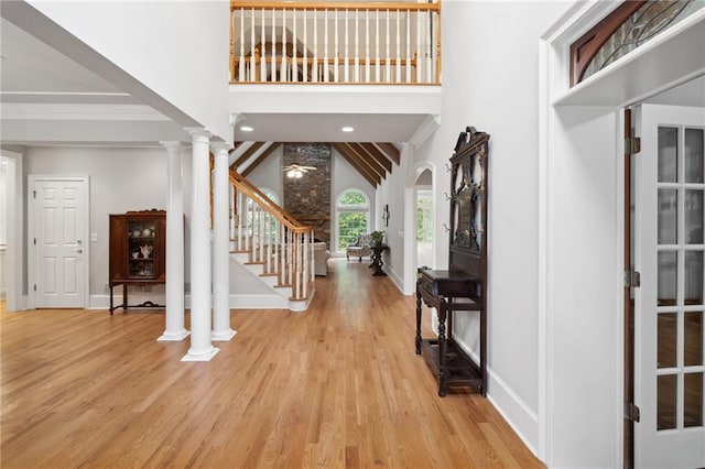 foyer with ornamental molding, stairway, arched walkways, a high ceiling, and ornate columns