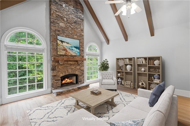 living room with a ceiling fan, wood finished floors, high vaulted ceiling, beam ceiling, and a stone fireplace