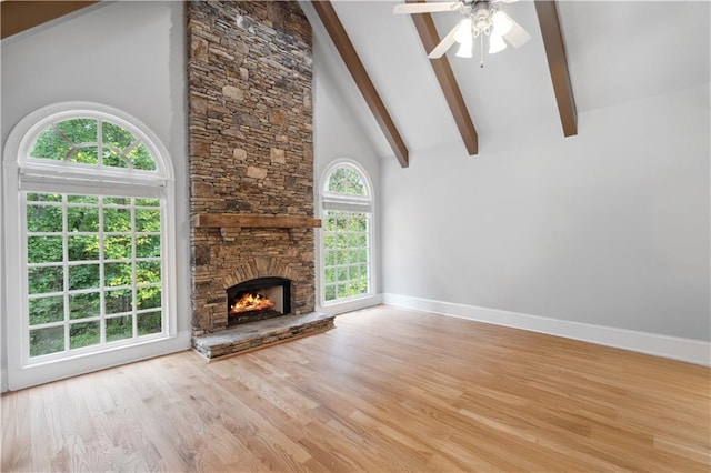 unfurnished living room featuring baseboards, beamed ceiling, a stone fireplace, wood finished floors, and high vaulted ceiling