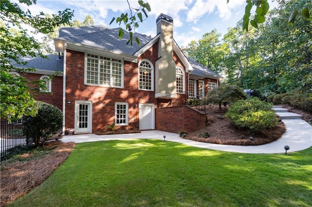 rear view of house with brick siding, a lawn, fence, and a chimney