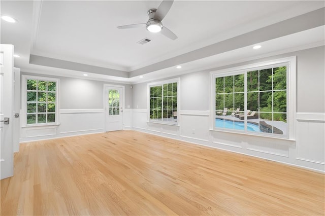 empty room with visible vents, light wood-style flooring, ornamental molding, a raised ceiling, and ceiling fan