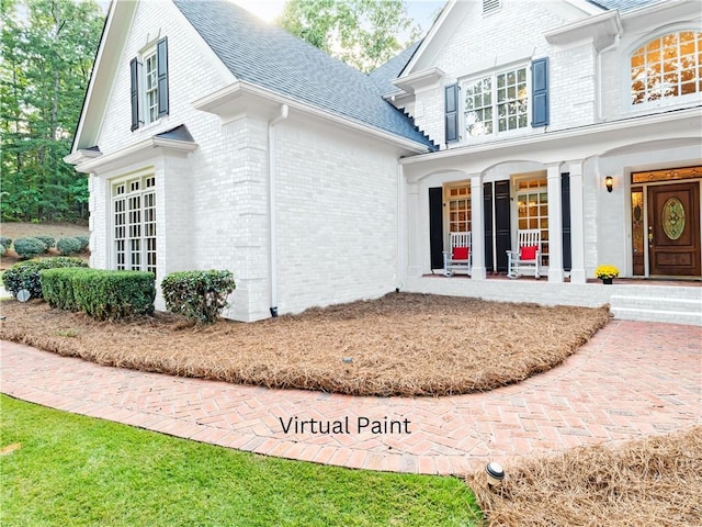 doorway to property featuring a porch, brick siding, and a shingled roof