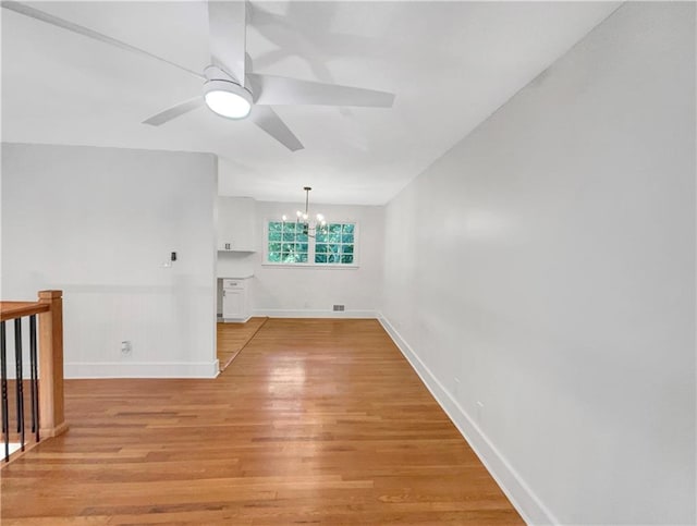 spare room with ceiling fan with notable chandelier and light wood-type flooring