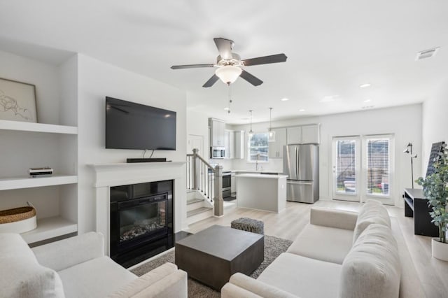 living room with ceiling fan, a healthy amount of sunlight, light wood-type flooring, and built in features