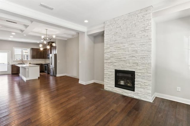 unfurnished living room with dark wood-style flooring, a sink, a stone fireplace, and baseboards