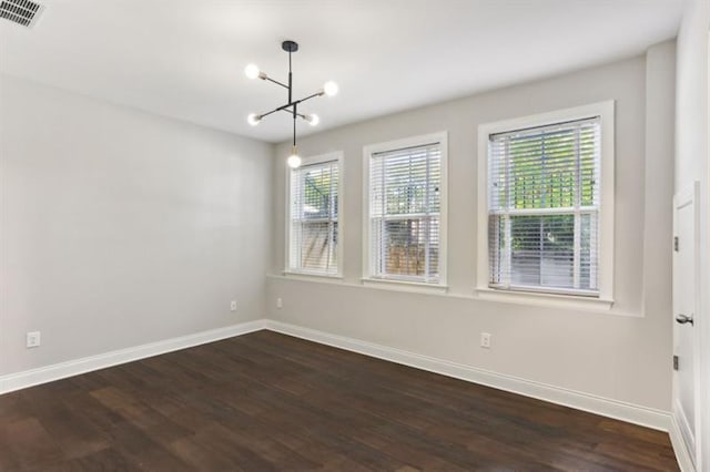 empty room featuring dark wood-style flooring, visible vents, baseboards, and an inviting chandelier