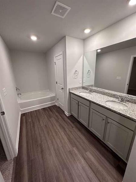 bathroom featuring visible vents, a garden tub, a sink, wood finished floors, and double vanity