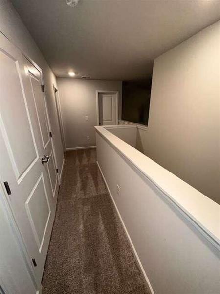 hall featuring an upstairs landing, dark carpet, and baseboards