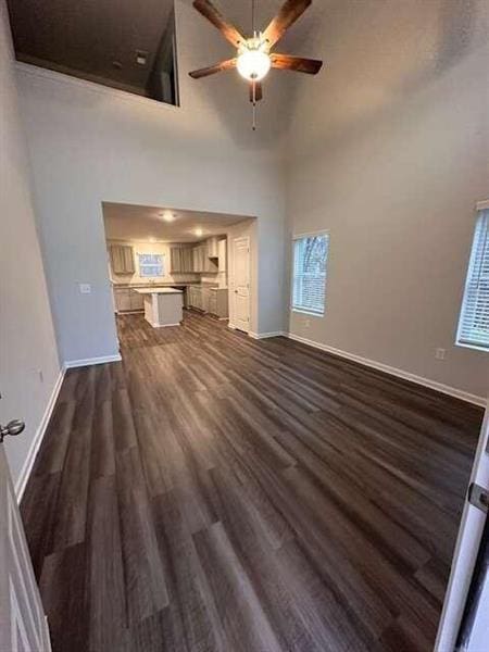 unfurnished living room featuring dark wood-type flooring, baseboards, a towering ceiling, and ceiling fan