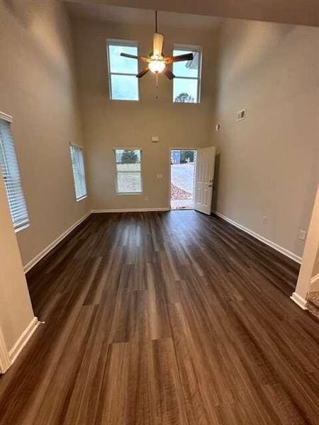 unfurnished living room featuring a ceiling fan, baseboards, dark wood-style flooring, and a towering ceiling