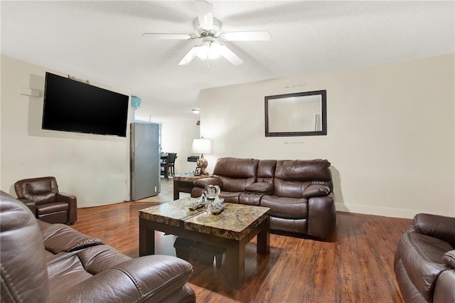 living room featuring dark wood-type flooring, ceiling fan, and a textured ceiling