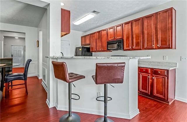 2555 Flat Shoals Rd Unit 2006, Atlanta, GA 30349 - kitchen with black appliances, dark wood-style floors, a breakfast bar area, a textured ceiling, and reddish brown cabinets