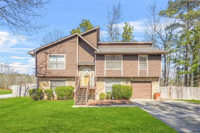 split foyer home with fence, stone siding, driveway, a garage, and a front lawn