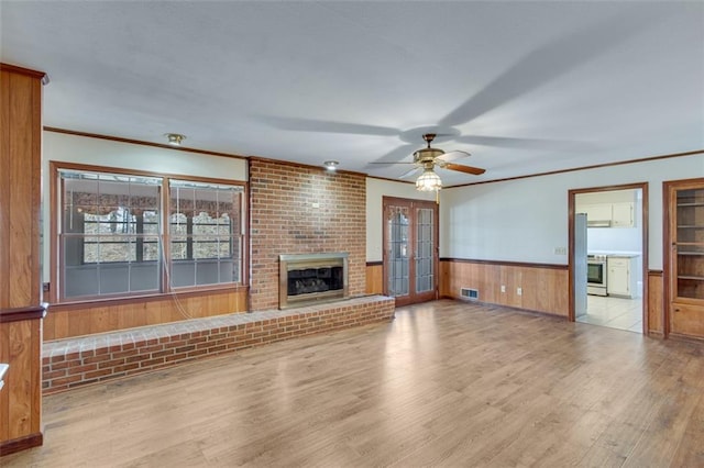 unfurnished living room with light wood-type flooring, ornamental molding, wooden walls, ceiling fan, and a fireplace