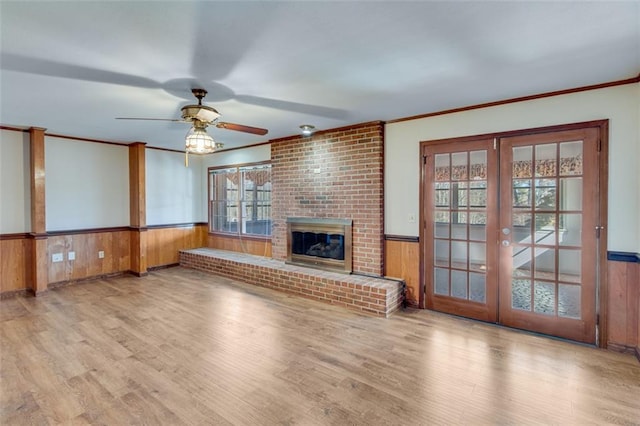 unfurnished living room featuring ceiling fan, ornamental molding, a brick fireplace, french doors, and light wood-type flooring