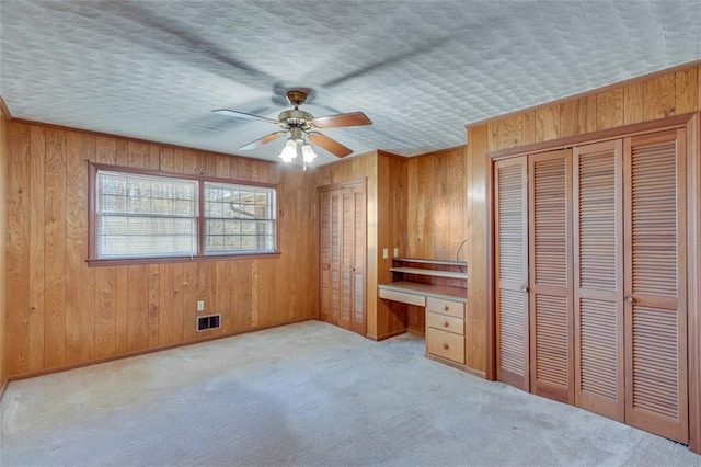 unfurnished bedroom featuring built in desk, a textured ceiling, ceiling fan, and wood walls