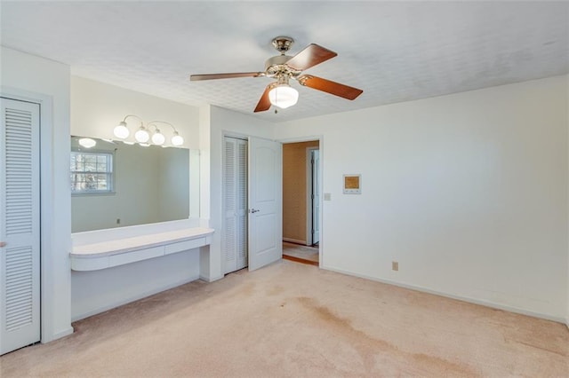 unfurnished bedroom featuring light carpet, multiple closets, a textured ceiling, and ceiling fan