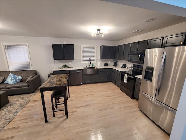 kitchen featuring light wood-style floors, a sink, light countertops, black appliances, and backsplash