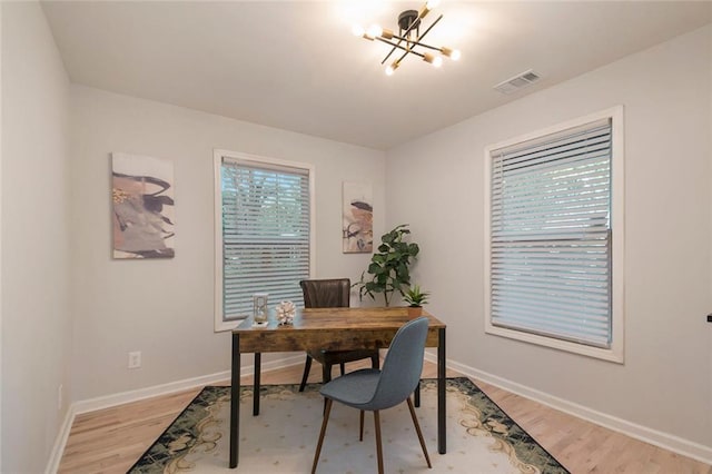 home office featuring light wood-style floors, baseboards, visible vents, and a notable chandelier