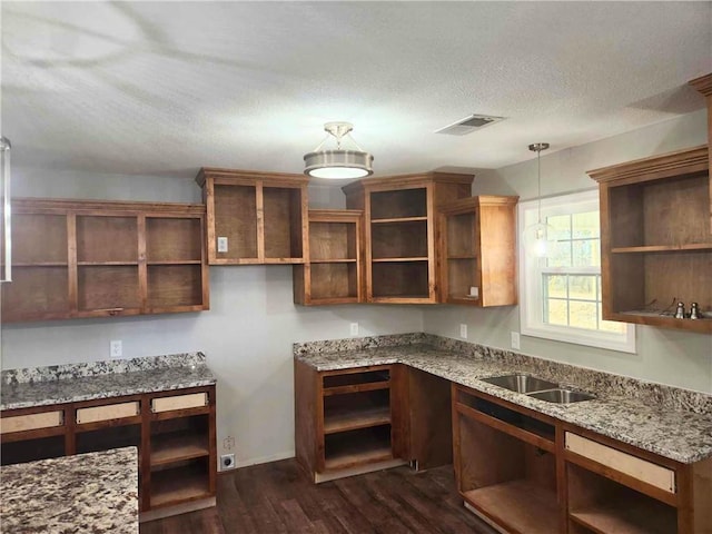 kitchen featuring sink, dark hardwood / wood-style flooring, hanging light fixtures, light stone countertops, and a textured ceiling