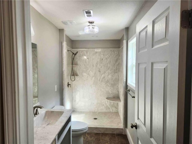 bathroom featuring vanity, a tile shower, tile patterned floors, and toilet