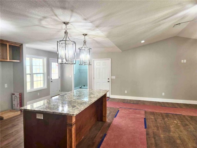 kitchen with a center island, light stone counters, dark hardwood / wood-style flooring, and decorative light fixtures