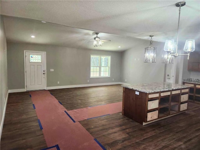 kitchen with dark wood-type flooring, ceiling fan, a kitchen island, and hanging light fixtures