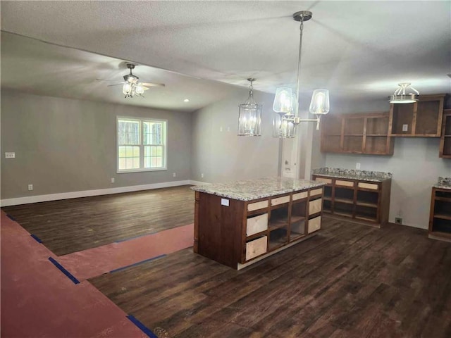 kitchen featuring dark wood-type flooring, light stone counters, a kitchen island, pendant lighting, and ceiling fan