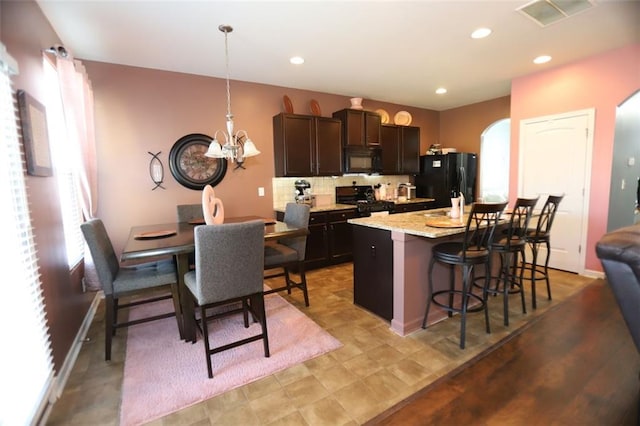 kitchen featuring tasteful backsplash, a notable chandelier, a breakfast bar, a center island with sink, and black appliances
